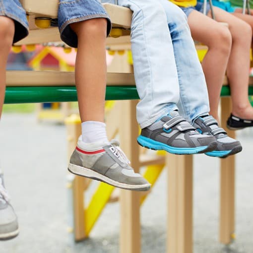 Children's legs and feet dangling from playground equipment - all with sneakers and shoes. Legs of little friends sitting on swing or other recreational facility.