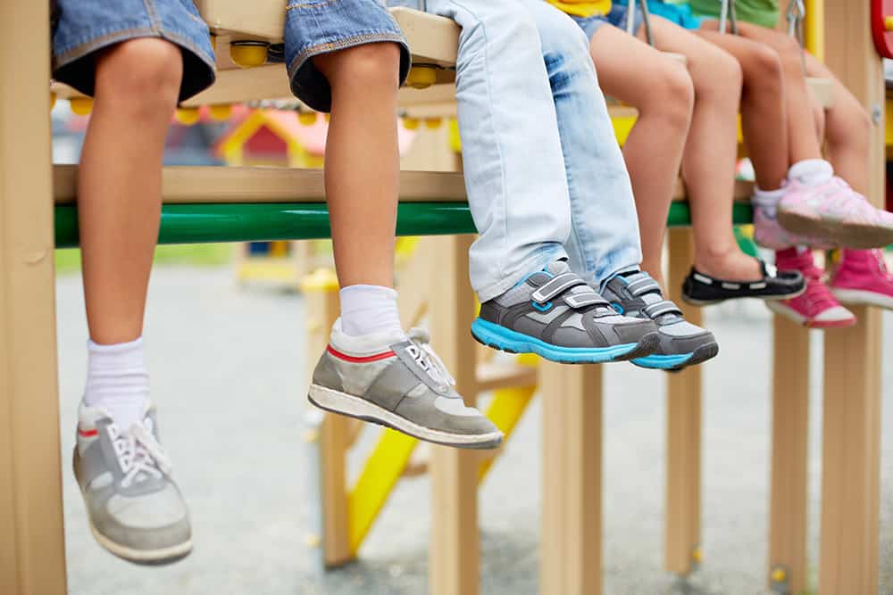 Children's legs and feet dangling from playground equipment - all with sneakers and shoes. Legs of little friends sitting on swing or other recreational facility.
