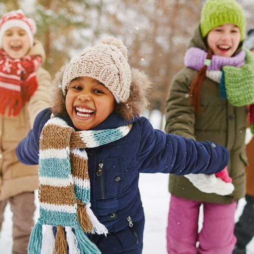 Happy kids playing outdoors with warm coats and snow pants thanks to Welcome to Winter.
