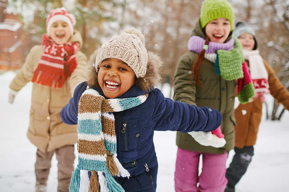 Happy kids playing outdoors in winter with their hats and mittens on
