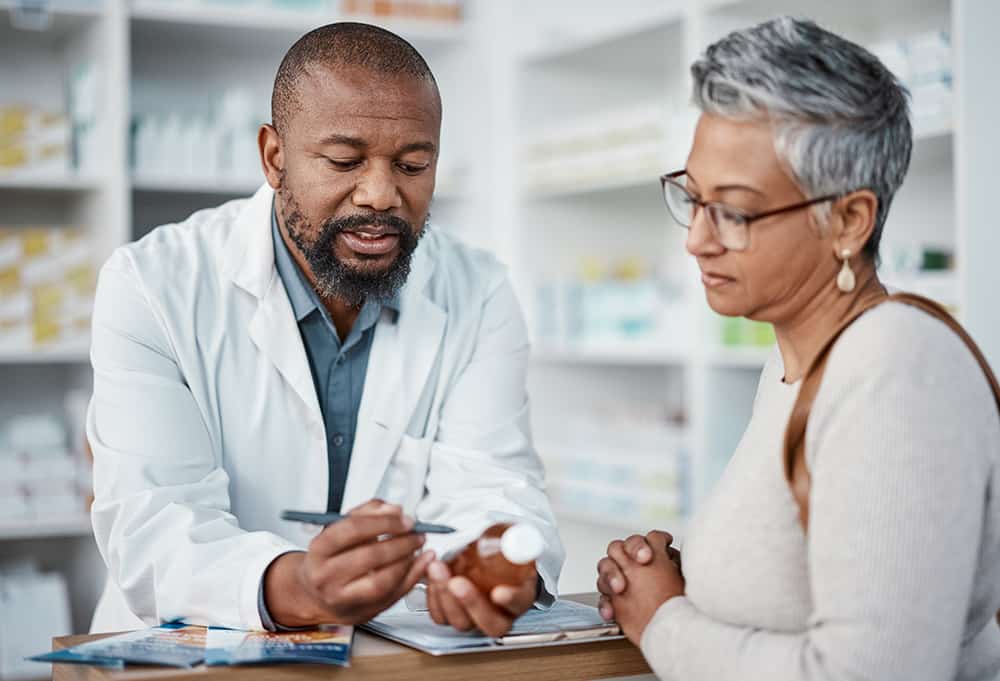 Pharmacy, black man and woman with healthcare medicine and conversation for instructions. Pharmacist, female patient or medical professional talking, stress or explain prescription to senior customer.